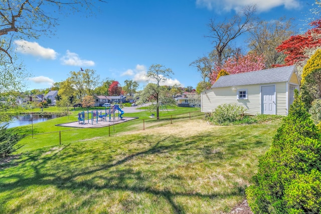view of yard with a water view, a playground, fence, and an outbuilding