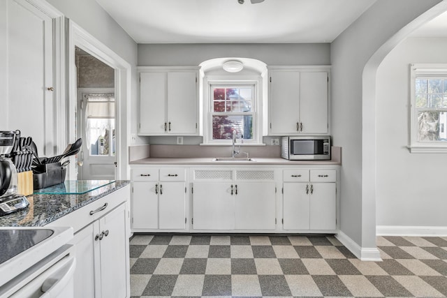 kitchen featuring a sink, arched walkways, white cabinets, and stainless steel microwave