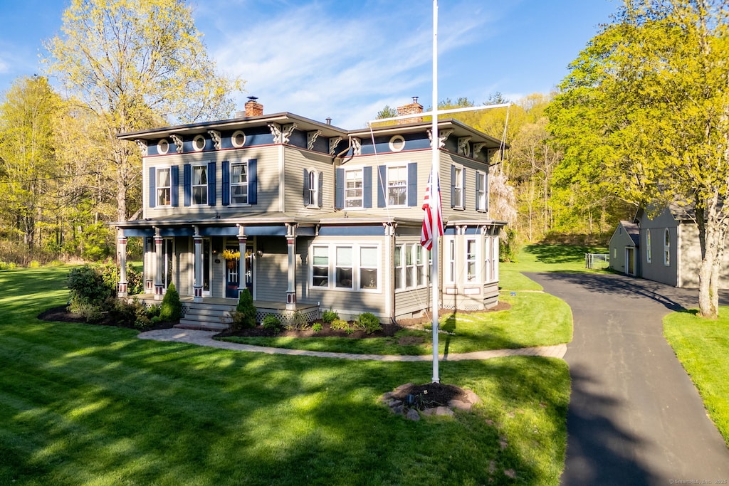 italianate-style house featuring covered porch, a chimney, and a front lawn