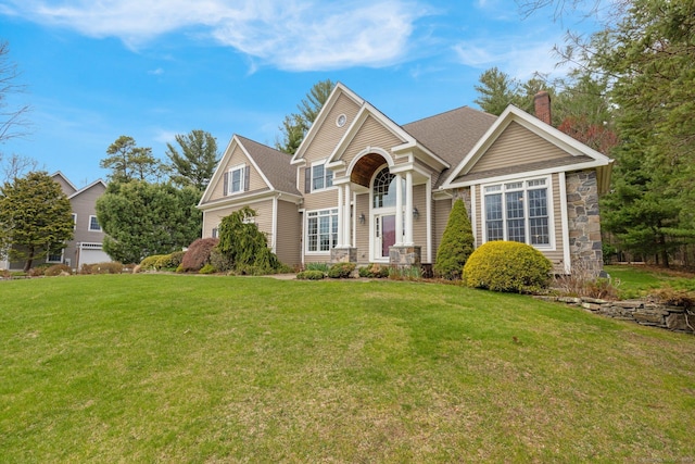 view of front of property with stone siding, a chimney, a shingled roof, and a front yard
