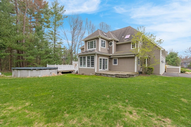 rear view of property with driveway, a covered pool, a yard, and a deck