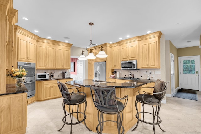 kitchen with dark stone counters, appliances with stainless steel finishes, light brown cabinets, and decorative backsplash