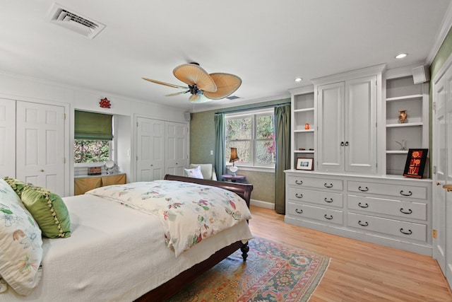 bedroom featuring crown molding, light wood finished floors, two closets, baseboards, and visible vents