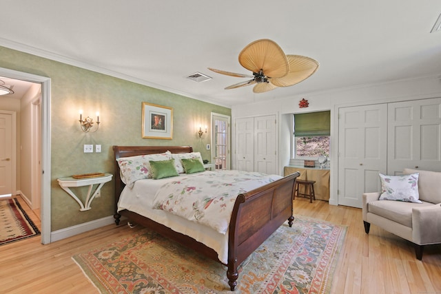 bedroom featuring crown molding, visible vents, multiple closets, light wood-type flooring, and a ceiling fan