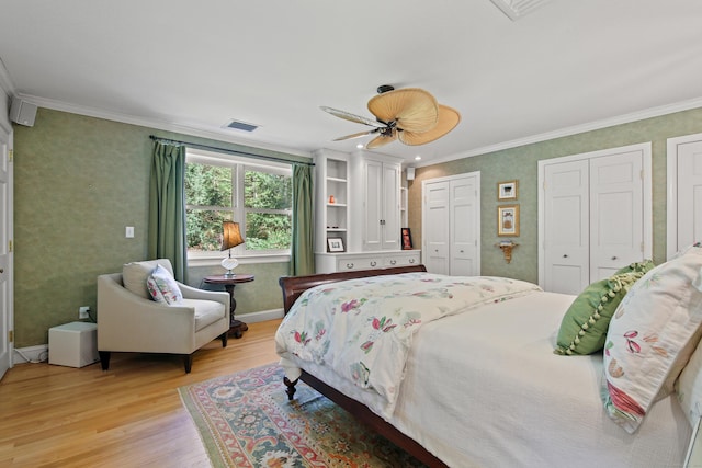 bedroom with crown molding, ceiling fan, two closets, light wood-type flooring, and visible vents