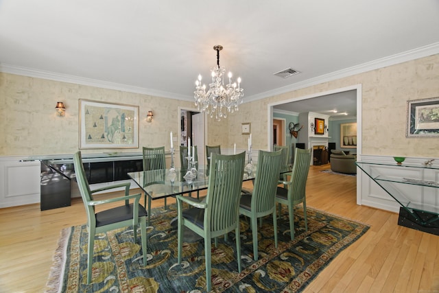 dining space featuring visible vents, a wainscoted wall, a chandelier, ornamental molding, and wallpapered walls