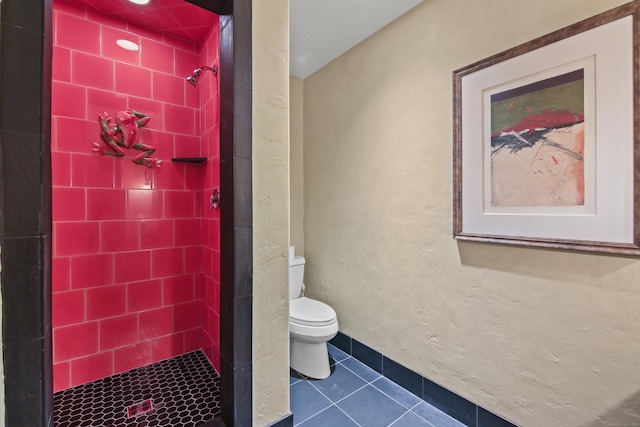 bathroom with tile patterned flooring, a textured wall, toilet, and a shower stall