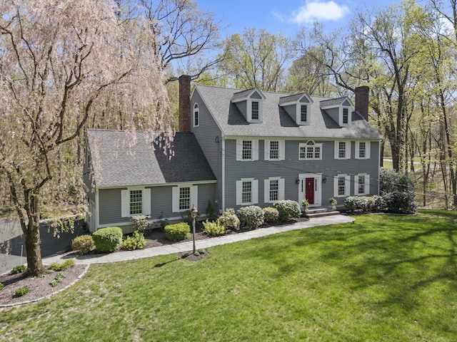 colonial-style house with a chimney, a shingled roof, and a front yard