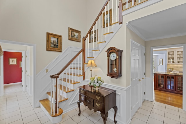stairs featuring tile patterned flooring, ornamental molding, a decorative wall, and a wainscoted wall