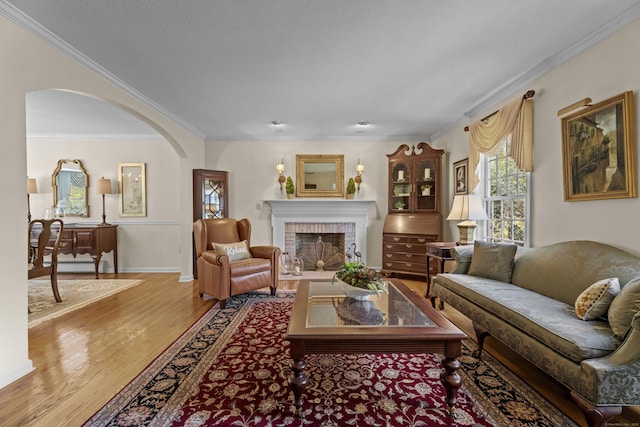 living area with a fireplace, arched walkways, baseboards, light wood-type flooring, and ornamental molding