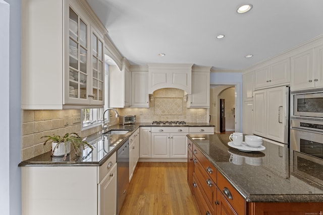 kitchen featuring glass insert cabinets, dark stone countertops, a sink, light wood-style flooring, and stainless steel appliances