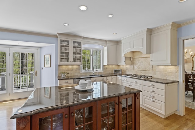 kitchen with a kitchen island, glass insert cabinets, light wood-type flooring, dark stone counters, and a sink