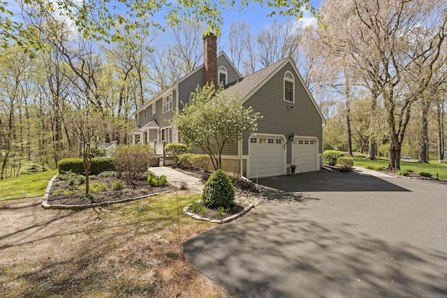 view of side of home featuring an attached garage, a chimney, and aphalt driveway