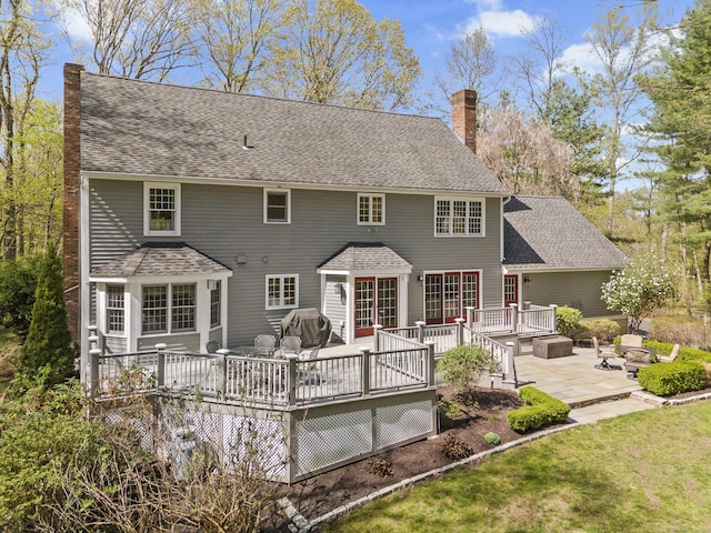 rear view of property featuring a shingled roof, an outdoor fire pit, a deck, a chimney, and a patio