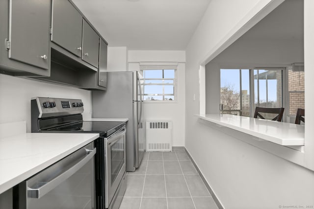 kitchen with light tile patterned floors, baseboards, gray cabinetry, radiator, and stainless steel appliances