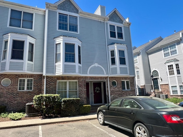 view of property with brick siding, cooling unit, and uncovered parking