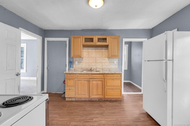 kitchen featuring white appliances, light wood-style floors, baseboards, a sink, and backsplash