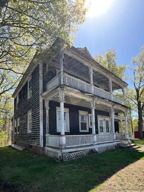 rear view of property featuring a lawn, a balcony, and covered porch
