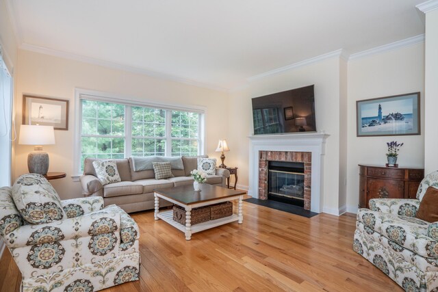 living area featuring crown molding, light wood finished floors, a brick fireplace, and baseboards