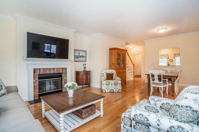 living area with stairway, crown molding, light wood finished floors, and a brick fireplace