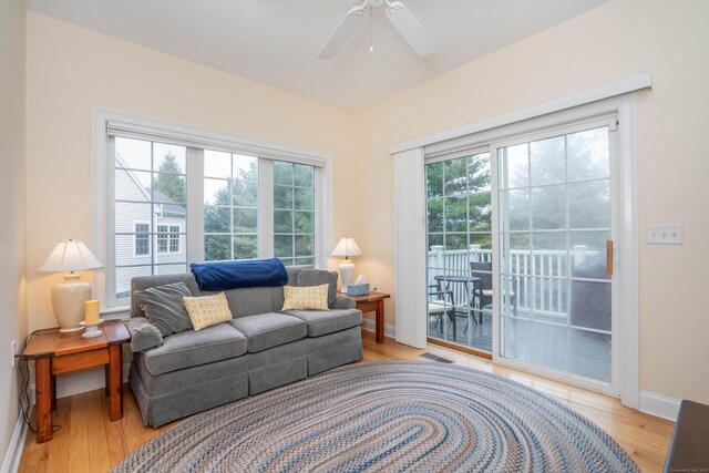 living area with baseboards, light wood-type flooring, and a ceiling fan
