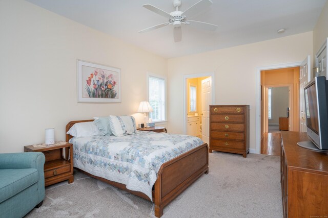 bedroom with light carpet, a ceiling fan, and ensuite bathroom