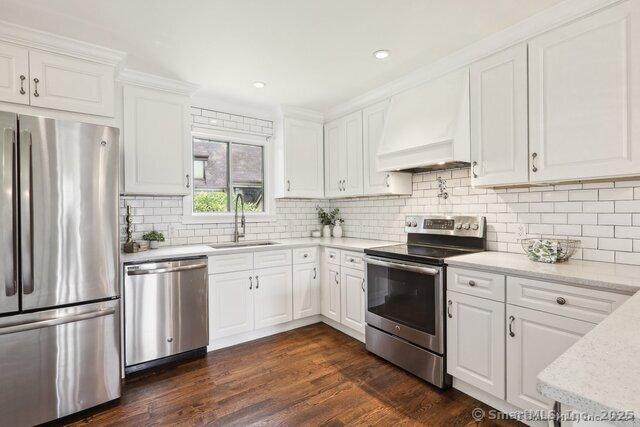 kitchen featuring stainless steel appliances, white cabinetry, a sink, and custom range hood