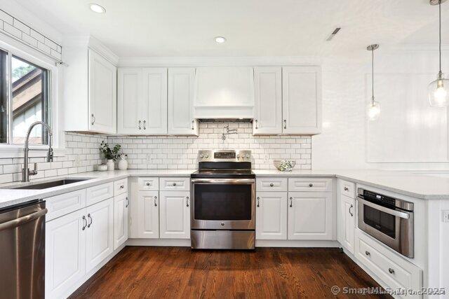 kitchen featuring appliances with stainless steel finishes, a sink, light countertops, custom range hood, and white cabinetry