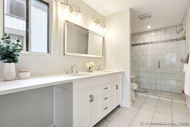 full bath featuring tile patterned flooring, double vanity, toilet, a shower stall, and a sink