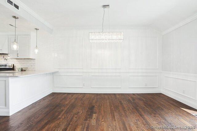 unfurnished dining area featuring crown molding, a decorative wall, dark wood-style flooring, and visible vents