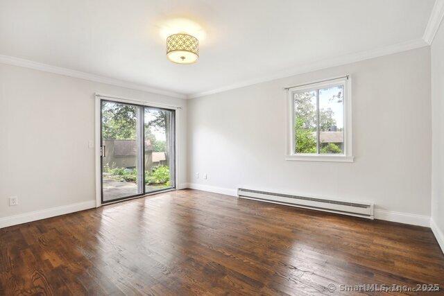unfurnished room with crown molding, a baseboard heating unit, a wealth of natural light, and wood finished floors