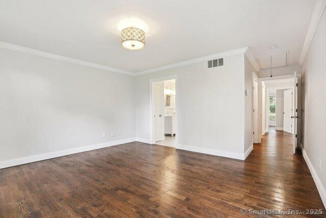 spare room featuring visible vents, attic access, wood finished floors, and ornamental molding