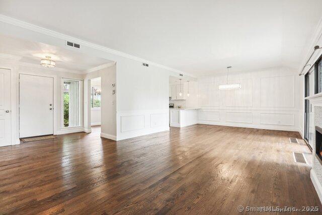 unfurnished living room with a fireplace, a decorative wall, wood finished floors, and visible vents