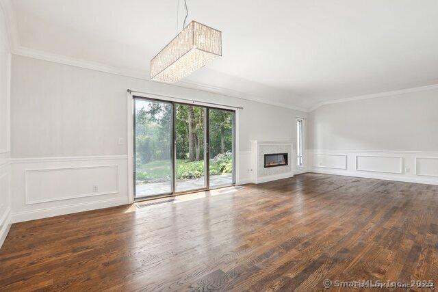 unfurnished living room featuring a glass covered fireplace, ornamental molding, a decorative wall, and wood finished floors