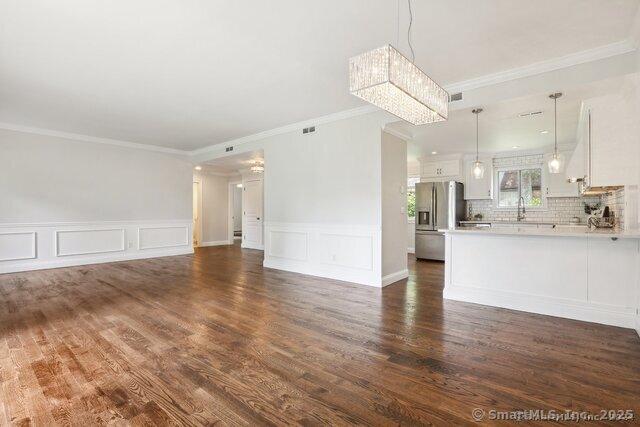 unfurnished living room featuring crown molding, visible vents, an inviting chandelier, a decorative wall, and dark wood-type flooring
