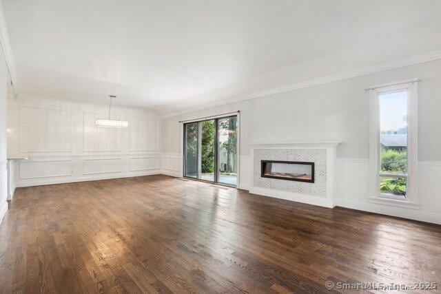 unfurnished living room featuring crown molding, a glass covered fireplace, wood finished floors, a decorative wall, and a wainscoted wall