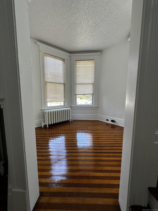 spare room with baseboards, a textured ceiling, radiator, and hardwood / wood-style flooring