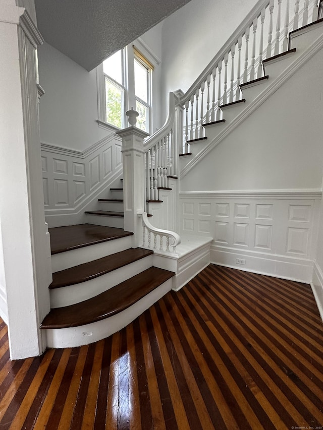 stairway with hardwood / wood-style floors, a wainscoted wall, and a decorative wall