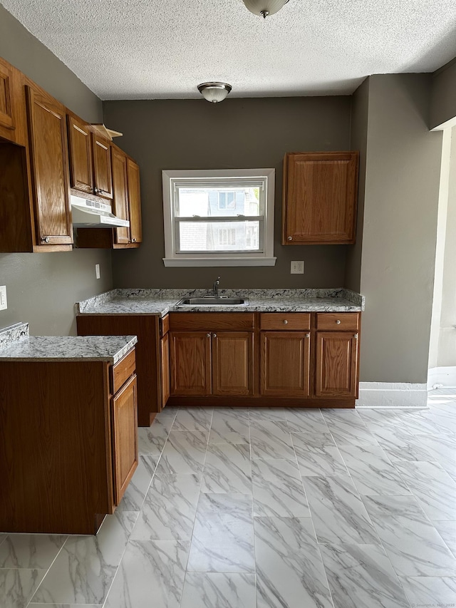 kitchen featuring a sink, marble finish floor, under cabinet range hood, and brown cabinets