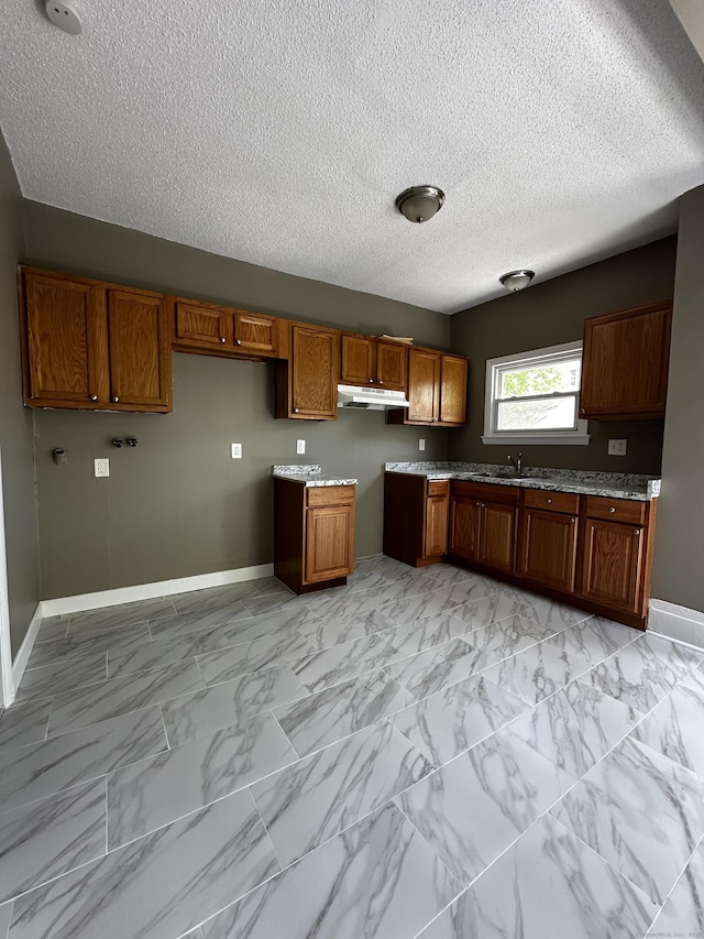 kitchen featuring marble finish floor, baseboards, a textured ceiling, brown cabinets, and a sink