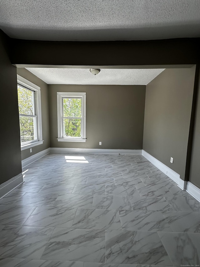 empty room with baseboards, marble finish floor, and a textured ceiling