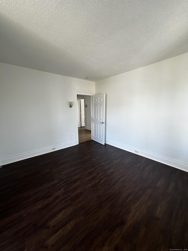 empty room with baseboards, dark wood finished floors, and a textured ceiling