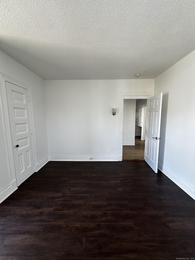 spare room with a textured ceiling, baseboards, and dark wood finished floors