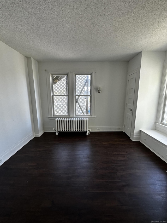 empty room featuring a healthy amount of sunlight, radiator, dark wood-style floors, and a textured ceiling