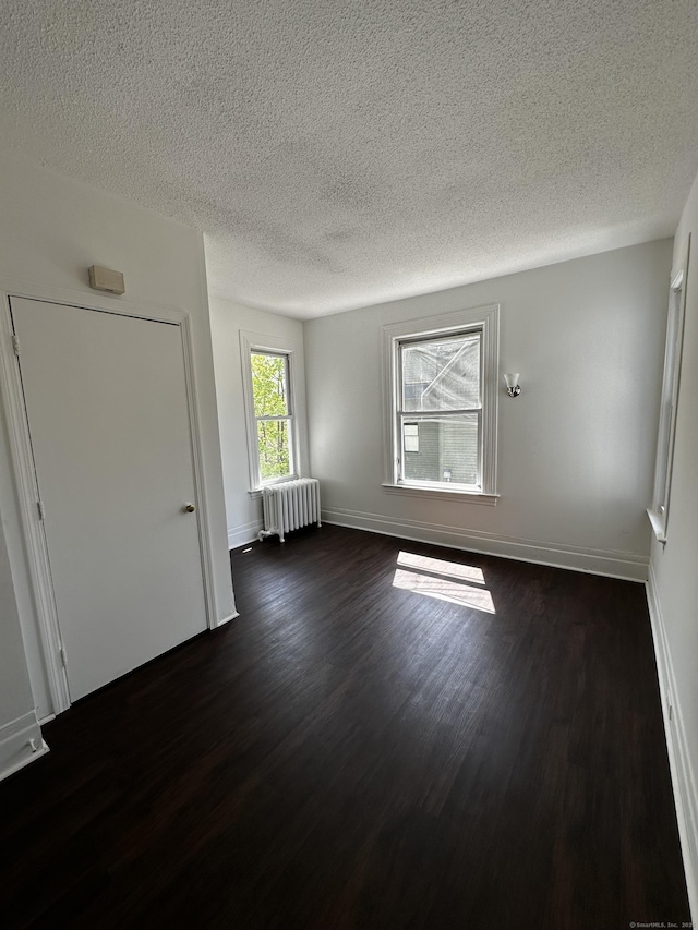 spare room featuring baseboards, a textured ceiling, radiator, and dark wood finished floors