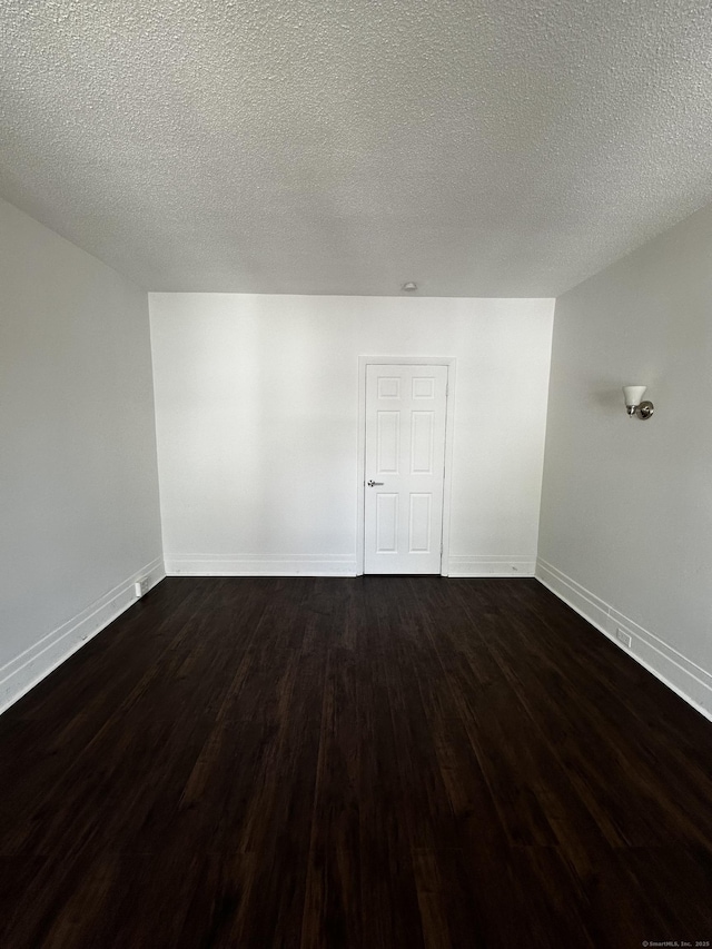 empty room with a textured ceiling, baseboards, and dark wood-type flooring