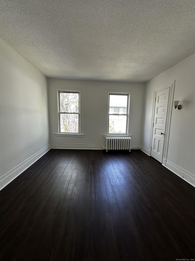 empty room with baseboards, a textured ceiling, radiator heating unit, and dark wood-type flooring