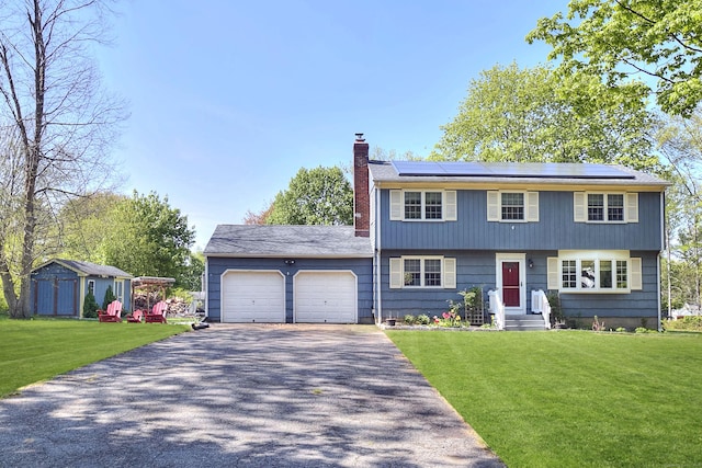 colonial-style house featuring an attached garage, driveway, a chimney, and a front yard