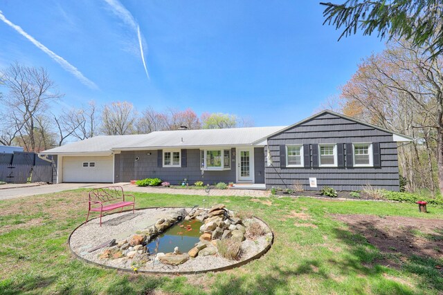 ranch-style house with a garden pond, an attached garage, driveway, and a front lawn