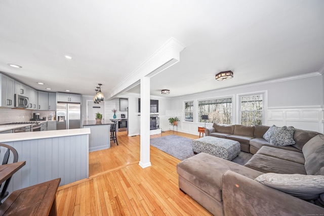 living room with ornamental molding, wainscoting, a decorative wall, a fireplace, and light wood-type flooring